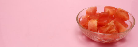 Clipped to banner size image of chopped tomato in a glass bowl isolated on a pink background.の写真素材
