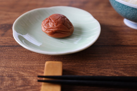 Pickled plum on a plate with rice on a wooden table.