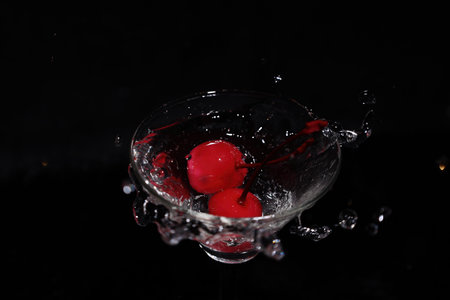 liquid splashing into a glass with cherries in a black background.
