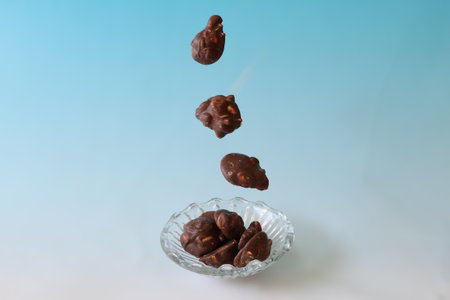 Chocolate balls falling in glass bowl on blue background with copy space