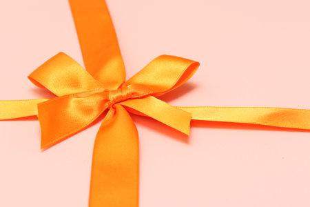 Orange ribbon with bow on a pink background. Place for text.