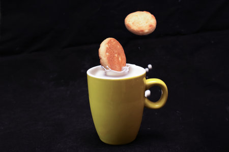 Cookies soaked with a yellow cup in milk in a black background.の写真素材