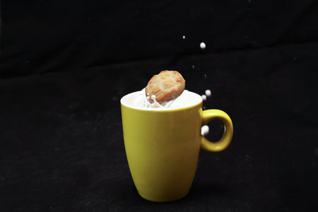 Cookies soaked with a yellow cup in milk in a black background.の写真素材