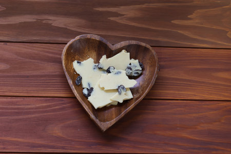 White chocolates with raisin on a heart shaped bowl in a wooden background.の写真素材