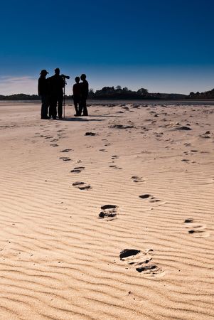 A group of people silhouetted against the blue sky meet late in the day on the beachの写真素材