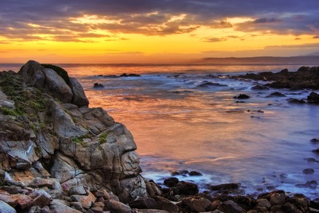 A beautiful sunrise is seen over the Monterey harbor with waves crashing in the foregroundの写真素材