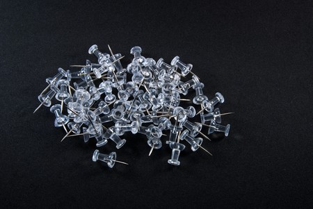 A group of clear plastic pushpins sit isolated on a black backgroundの写真素材