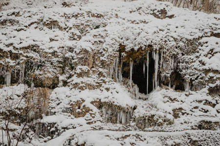 Wild river in the forest in winter with rocks and a stream of water and sandy cliffs with ice freezes and iciclesの写真素材