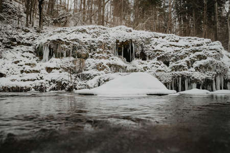 Wild river in the forest in winter with rocks and a stream of water and sandy cliffs with ice freezes and iciclesの写真素材