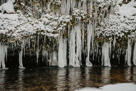 Wild river in the forest in winter with rocks and a stream of water and sandy cliffs with ice...