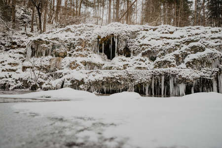 Wild river in the forest in winter with rocks and a stream of water and sandy cliffs with ice freezes and iciclesの写真素材