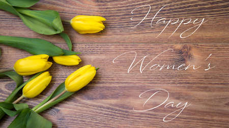 happy womens day text sign on tulips on brown wooden rustic background. stylish flat lay with flowers and drink with space for text. greeting card. hello spring.の写真素材