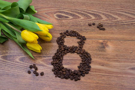 Yellow tulips on a dark wooden background with coffee beans in the form of March 8. Greeting card...