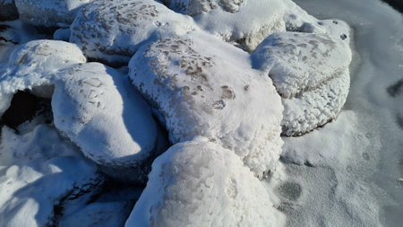 Close-up of frozen sea stones by the sea. cool winter day. A layer of white snow over the stonesの写真素材