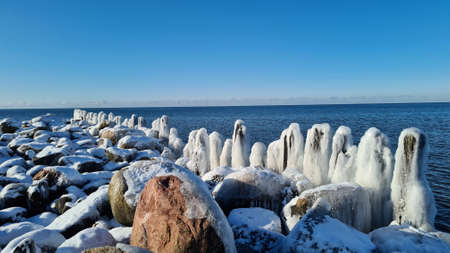 frozen wooden poles on the sea shore with blue water and blue sky on a sunny winter day. winter landscapeの写真素材