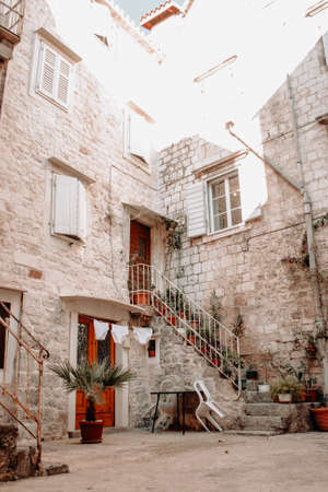 beautiful view of Croatian town houses. An old stone house with stairs on which there are many flower pots. Women's underwear dries on the laundry rope. In the yard of the house is a sitting table with plastic chairs. City viewの写真素材