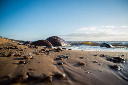 Close-up of small pebble pebbles on the sea shore in the sand with large boulders in a blurred...