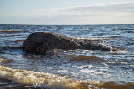huge rock on the sea shore in the water, which is washed by the sea water and the waves splash against it. Warm spring evening mood by the sea.Spring landscapeの写真素材