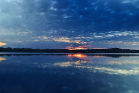 Sunset sky background. Dramatic gold sunset with evening sky clouds over the lake. Stunning sky clouds in the sunrise. Sky landscape. Panoramic view. Summer landscapeの写真素材