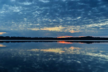 Sunset sky background. Dramatic gold sunset with evening sky clouds over the lake. Stunning sky clouds in the sunrise. Sky landscape. Panoramic view. Summer landscapeの写真素材
