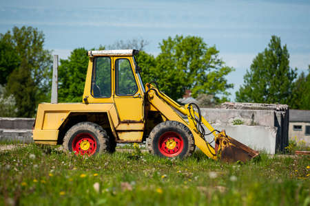Yellow excavator with red discs on a green grass against the blue skyの写真素材