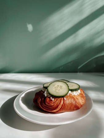 On a white plate with a bowl of cottage cheese and freshly sliced green cucumber on a white table with a green wall. The sun's rays are reflected on the wall.の写真素材
