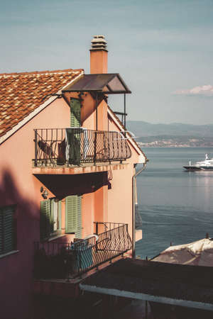 Pink residential house with balconies bounded by a metal structure. In the background a yacht and Croatian mountains.の写真素材