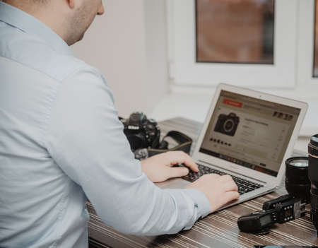 Men search new photo camera on computer, using  laptop also. He is a freelance photographer. Photo...