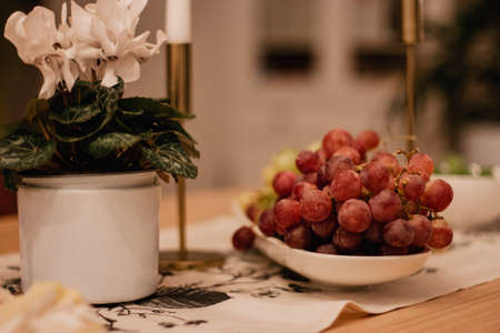 Red grapes on a white plate on a decorated holiday table next to a flower in a pot.の写真素材