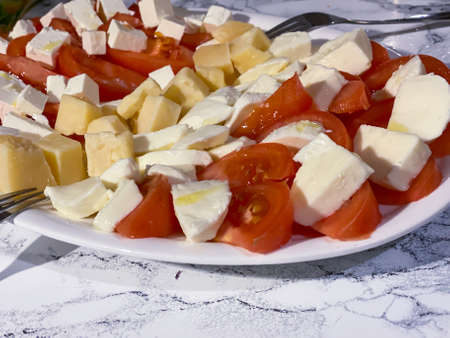 Sliced red tomato and feta, mozzarella cheese on a white plate. Healthy snack.