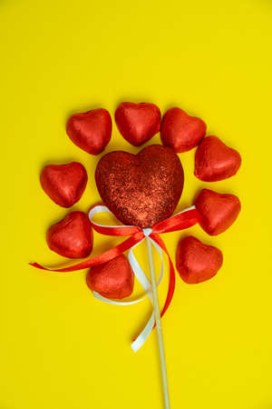 Chocolate red heart sweets for Valentine's Day on a yellow background in the shape of a circle with a heart decoration on a wooden pole in the middle.の写真素材