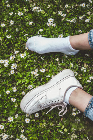 youth sneakers on girl legs and white sock on grass during sunny serene summer day.の写真素材