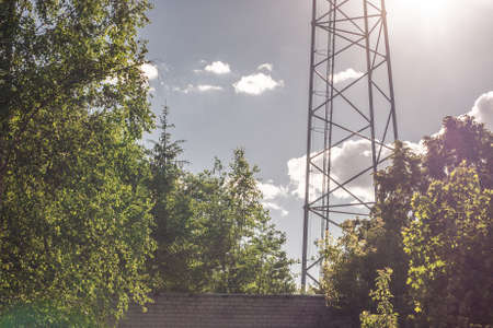 warm summer day with green trees and a brick wall next to a metal TV tower with antennas.の写真素材