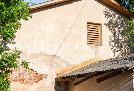 The wall of the house with a dilapidated plaster, with orange bricks at the bottom. Sunny summer day