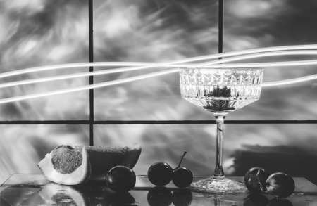 Crystal glass for cocktails on a glass surface. Fruits - grapes, grapefruit next to the glass. Abstract background.の写真素材