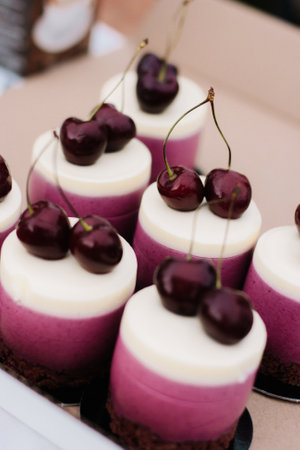 Delicious pink cake cupcakes with white frosting and a red cherry on top with a chocolate base.