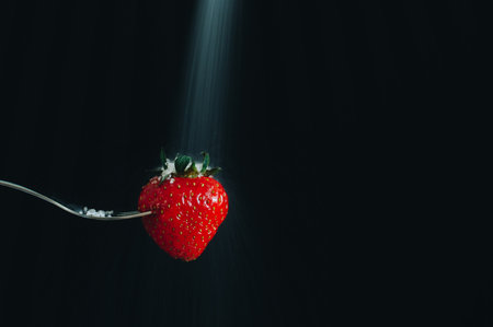 fresh ripe red strawberries impaled on a silver fork and sugar falling on it. black background. long exposure, selective focusの写真素材