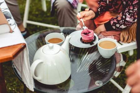 woman is enjoying a cupcake with a chocolate base and violet icing standing on a beautiful glass table. A white coffee mug is next to it.の写真素材