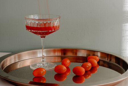 beautiful crystal glass with red tomatoes pouring a red tomato stalk stands on a gold-plated metal tray illuminated by sunlight casting a shadow on a white wall.の写真素材