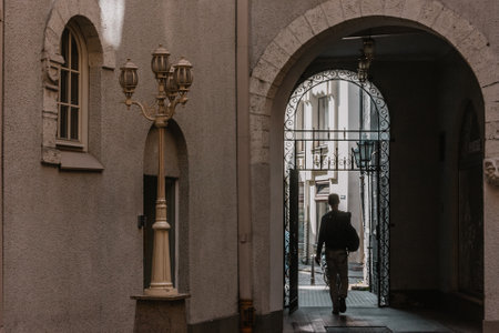 wall of a house with an arch through which a man with a bag passes. A golden chandelier lamp next to the arch.の写真素材