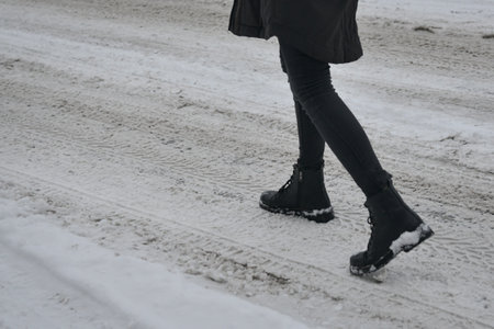 Woman's legs in high black boots walking down the street in the snow
