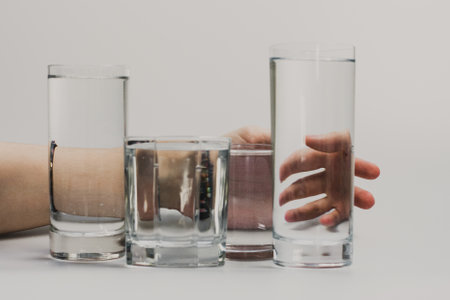 Still life with a woman's hand on a white background, in front of which are glass glasses with water, creating an illusion.の写真素材