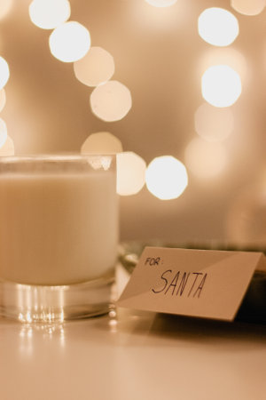 Christmas greeting card with a glass of milk left for Santa with Christmas bokeh lights in the...