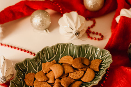 Christmas greeting card with gingerbread in a green dish surrounded by a red Santa's hat and Christmas decorations on a white table.の写真素材