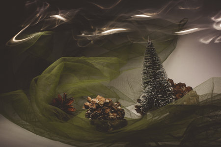 Christmas and New Year's card with a small artificial green tree and cones on a table with a colorful background in which lights shine, creating a bokeh background.の写真素材