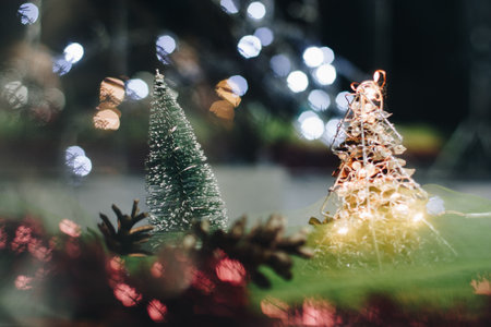 Christmas and New Year's card with a small artificial green tree and cones on a table with a colorful background in which lights shine, creating a bokeh background.の写真素材