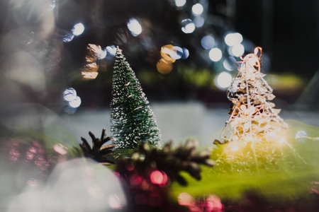 Christmas and New Year's card with a small artificial green tree and cones on a table with a colorful background in which lights shine, creating a bokeh background.の写真素材
