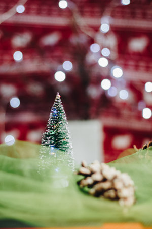 Christmas decorations with a green artificial Christmas tree and a cone wrapped in green fabric with a red background in which bokeh lights shine.の写真素材