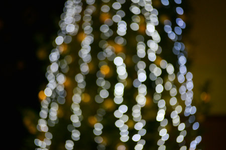 Blurred multicolored lights of a garland and branches of a Christmas tree in the foreground.Christmas and New Year background.Selective focus,copy space.の写真素材