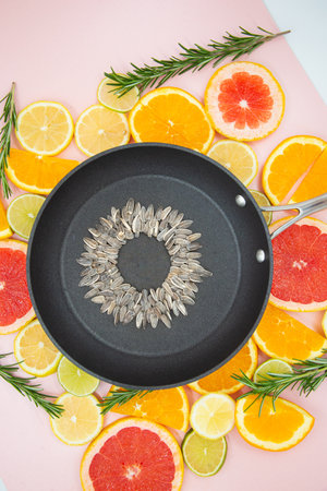 background of slices of citrus fruits, oranges, lemons, limes, grapefruits, on which a black pan is placed, inside which a sunflower flower is made from sunflower seeds. View from the top.の写真素材